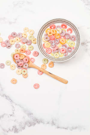 Fruit flavor colored cereals in a bowl with milk on a kitchen marble counter in a top view