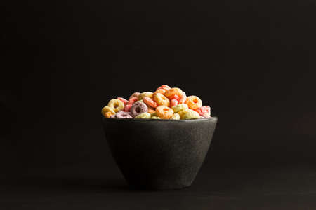 Fruit flavor colored cereals in a black bowl on a black background with copy spaceの写真素材