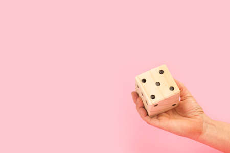 Woman hand holding a big wooden dice on a pink background with copy spaceの写真素材