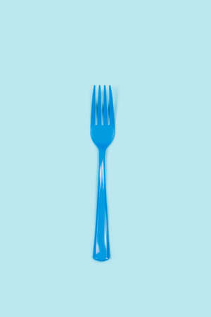 Disposable blue plastic fork on a light blue background with copy space