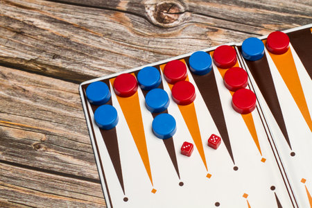 A backgammon board with red and blue checkers and small dice on a wooden table