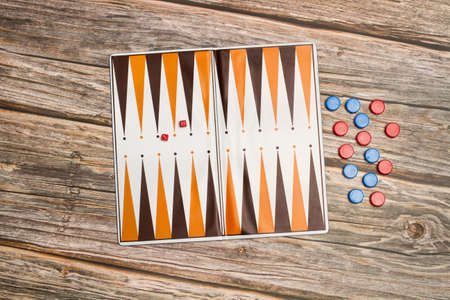 A backgammon board with red and blue checkers and small dice on a wooden table