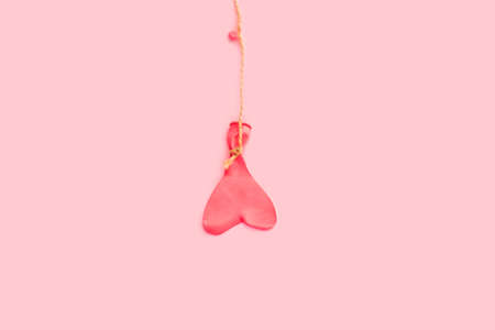 A heart shape deflated pink balloon hanging from a sisal thread on a pink background with copy spaceの写真素材