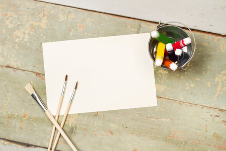 Wooden artistic paintbrushes, paint bottles and a sheet of paper on a wooden tableの写真素材