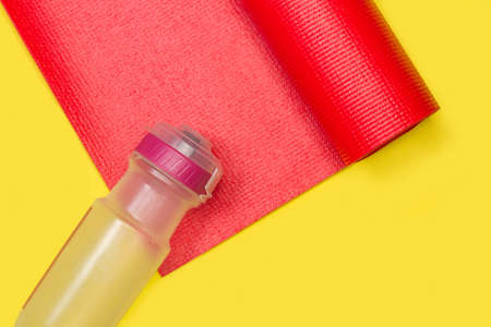 A plastic sport bottle on a red yoga mat on a yellow background in a top viewの写真素材