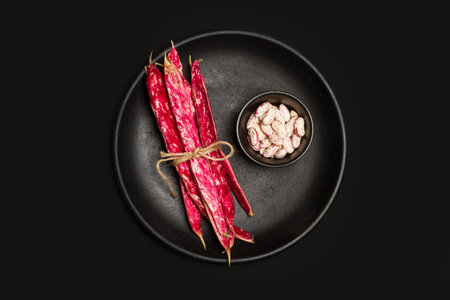 Pinto beans in a black bowl and on a black plate on black background in a top view