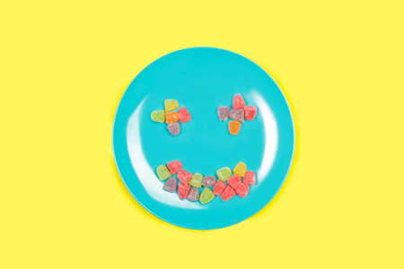 Colored gummies on a blue plate on a yellow background with copy spaceの写真素材