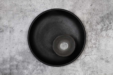 Black round dish and a dark bowl on a stone background in a top viewの写真素材