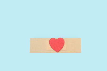 A red paper heart on an adhesive bandage on a light blue background with copy spaceの写真素材