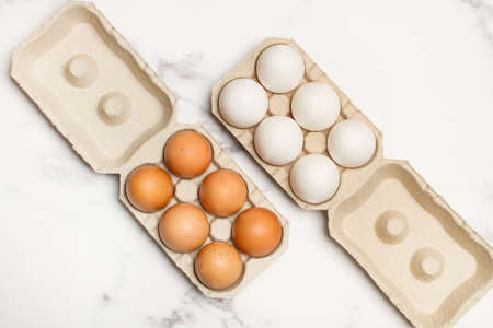 Brown and white eggs in cardboard egg holders on a marble background in a top view