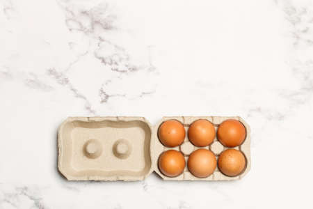 Six brown eggs in cardboard egg holder on a marble background in a top viewの写真素材