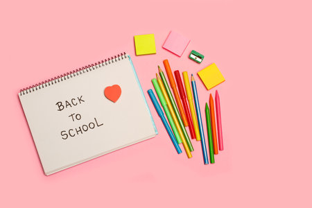Back to school write in a notebook, colored pencils and markers on a pink background with copy space