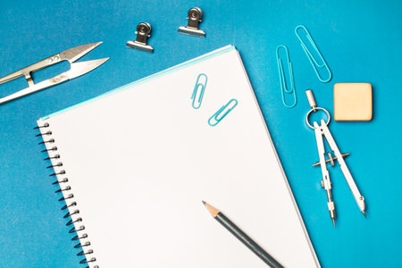 Open blank notebooÄ· and student utensils on a blue background