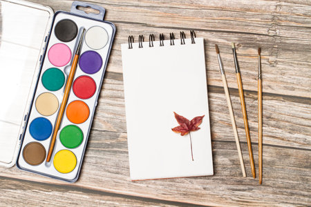 A palette of watercolors and paintbrushes on a wooden table in a top viewの写真素材