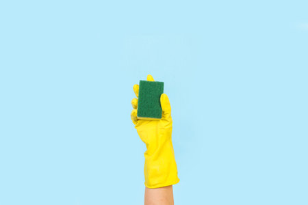 Woman hand with yellow rubber glove holding a cleaning sponge on a light blue background with copy spaceの写真素材