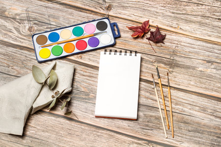 A palette of watercolors and paintbrushes on a wooden table in a top viewの写真素材
