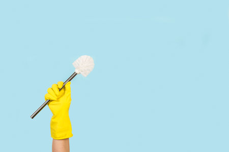 Woman hand with yellow rubber glove holding a toilet brush on a light blue background with copy spaceの写真素材