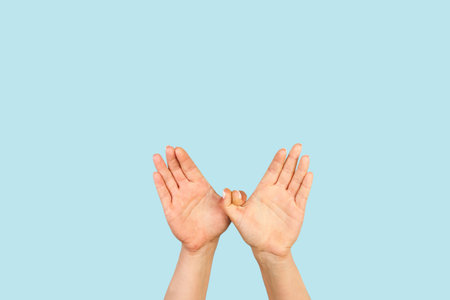 Woman hands in bird gesture on a light blue background with copy space