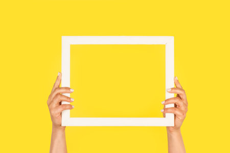 Woman hands showing a white picture frame on a yellow background with copy spaceの写真素材