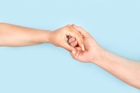 Man hand holding woman hand on a light blue background with copy spaceの写真素材