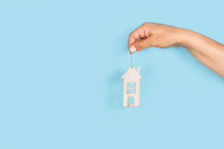 Woman hand holding a white wooden toy house on a light blue background with copy spaceの写真素材