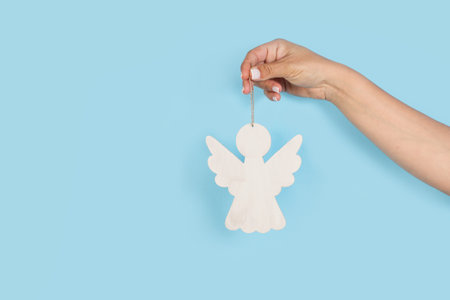Woman holding a white wooden angel on a light blue background with copy spaceの写真素材