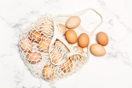 Brown eggs in a cotton mesh bag on a marble kitchen countertop in a top viewの写真素材