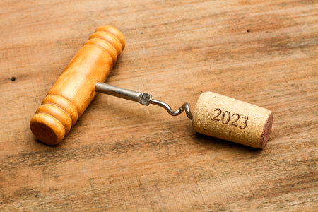 A corkscrew and a cork with 2023 number on a wooden background
