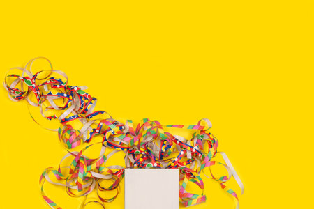 A white gift box and colored paper streamers on a yellow background with copy spaceの写真素材