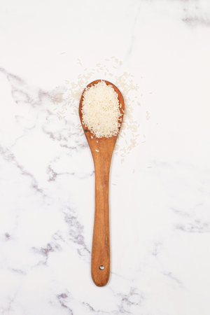 Raw rice in a wooden spoon and on a marble kitchen countertop in a top viewの写真素材