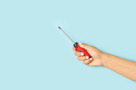 Woman hand holding a screwdriver on a light blue background with copy spaceの写真素材