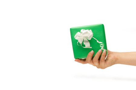 Woman hand holding a green gift box with a white ribbon on a white background with copy spaceの写真素材