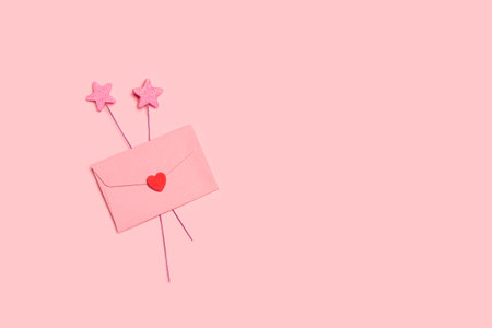 A pink envelope with a red paper heart and star decoration on a pink background with copy spaceの写真素材
