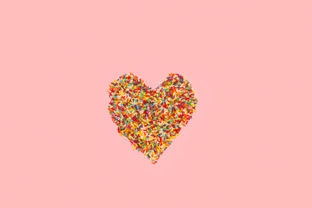 Sweet colored sprinkles in heart shape on a pink background with copy space