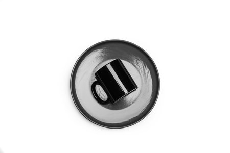 A black mug on a gray plate on a white background with copy space in a top view