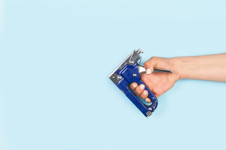 Woman hand holding a blue stapler gun on a white background with copy space