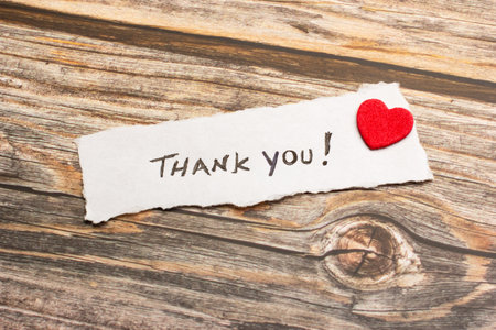 A piece of paper with thank you phrase and a red heart on a wooden backgroundの写真素材