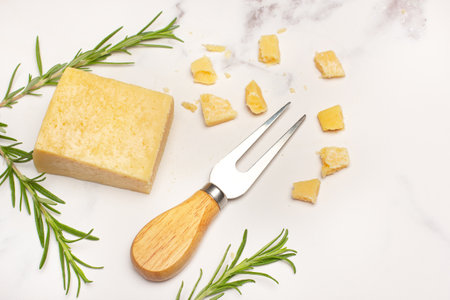 A piece of parmesan cheese, a fork and rosemary twigs on a white and gray marble counter in a top viewの写真素材