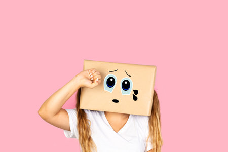 Woman with his head in a box and crying gesture standing on a pink background with copy spaceの写真素材