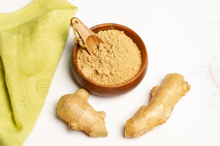 Parts of a ginger powder in a wooden bowl and a ginger root on a white background with copy spaceの写真素材