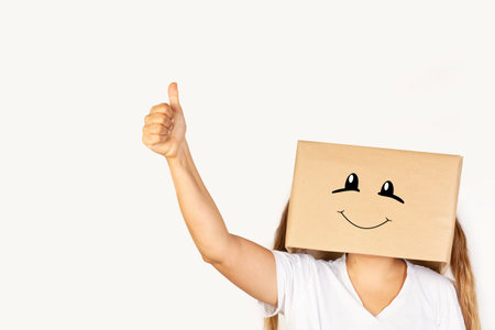 Woman with her head in a box, smile gesture and thumb up gesture standing on a white background with copy spaceの写真素材