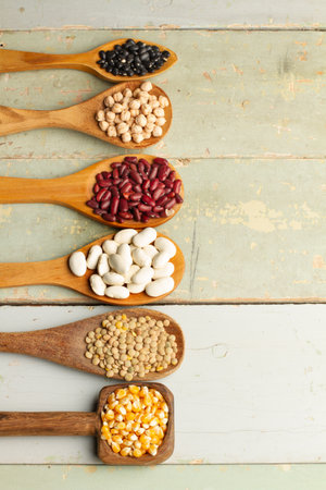 Red, black and white beans, chickpeas, lentils and corn kernels on wooden spoons and on a green...
