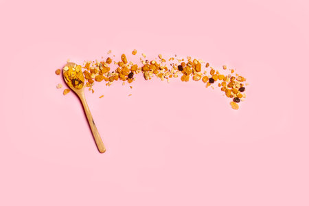 A heap of granola on a wooden spoon and on a pink background with copy space