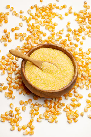 Cornmeal in a wooden bowl and corn kernels on a white background in a top viewの写真素材