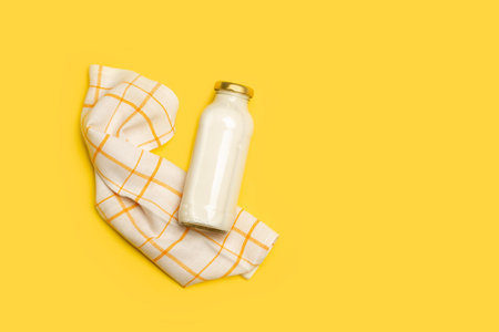 A bottle of milk and a square napkin on a yellow background with copy space in a top viewの写真素材