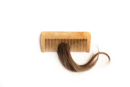A brown lock of hair and wooden comb on a white background with copy space