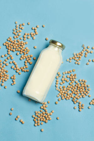 Soy milk bottle and soy beans on a light blue background in a top viewの写真素材