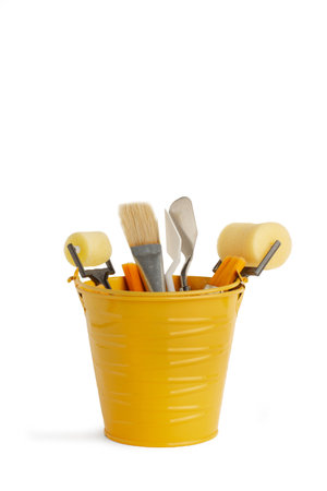 Paint brushes, paint rollers and spatulas in a yellow metal bucket on a white background with copy spaceの写真素材