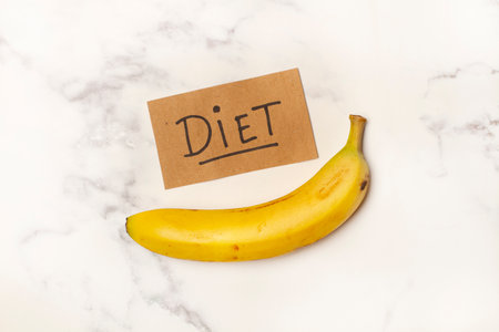 One banana with a diet sign on a white and gray marble kitchen counter in a top viewの写真素材