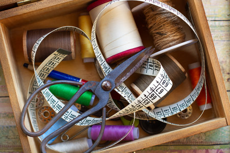 Thread, scissors and a measuring tape in a wooden box on a wooden table in a top view